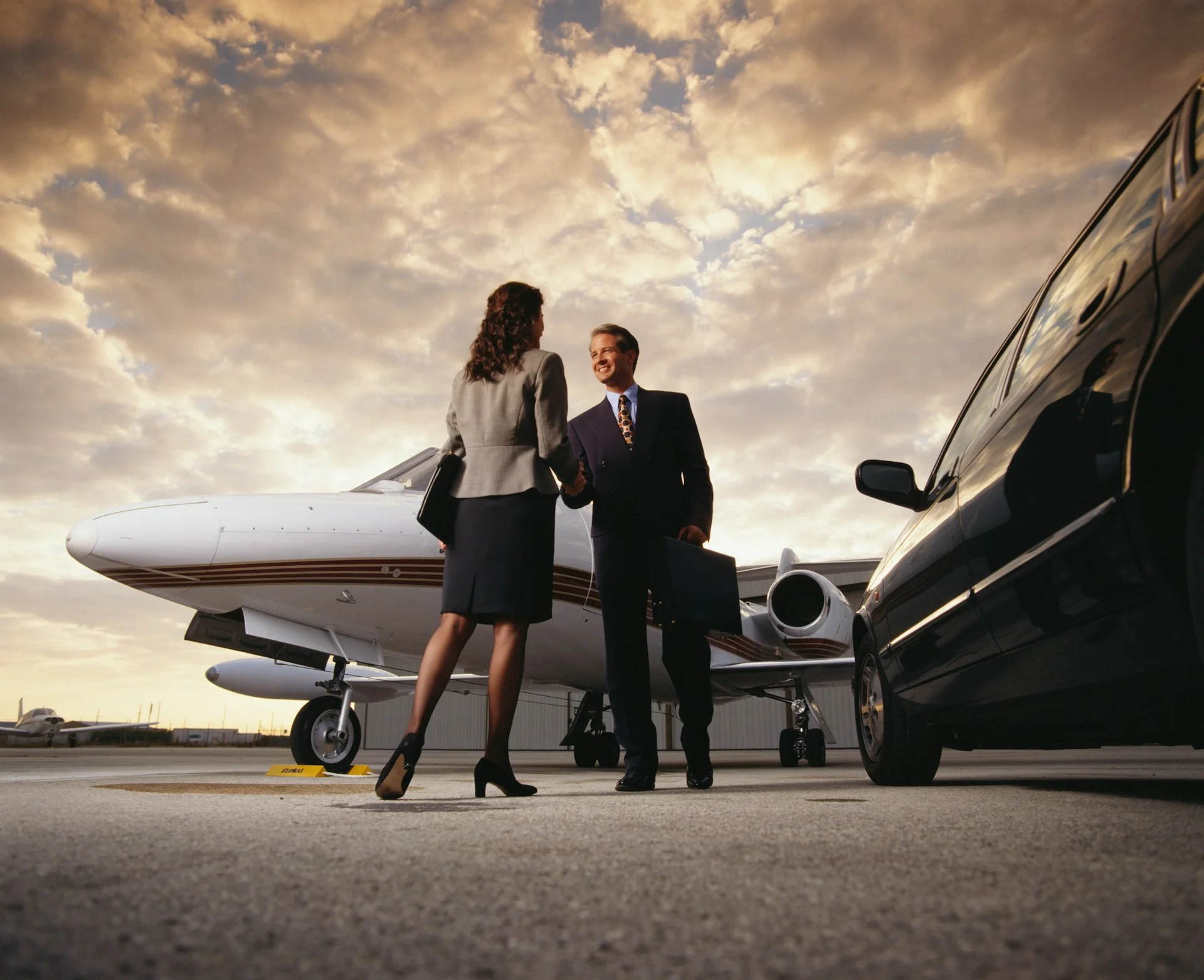 man and woman shaking hands with plane in background