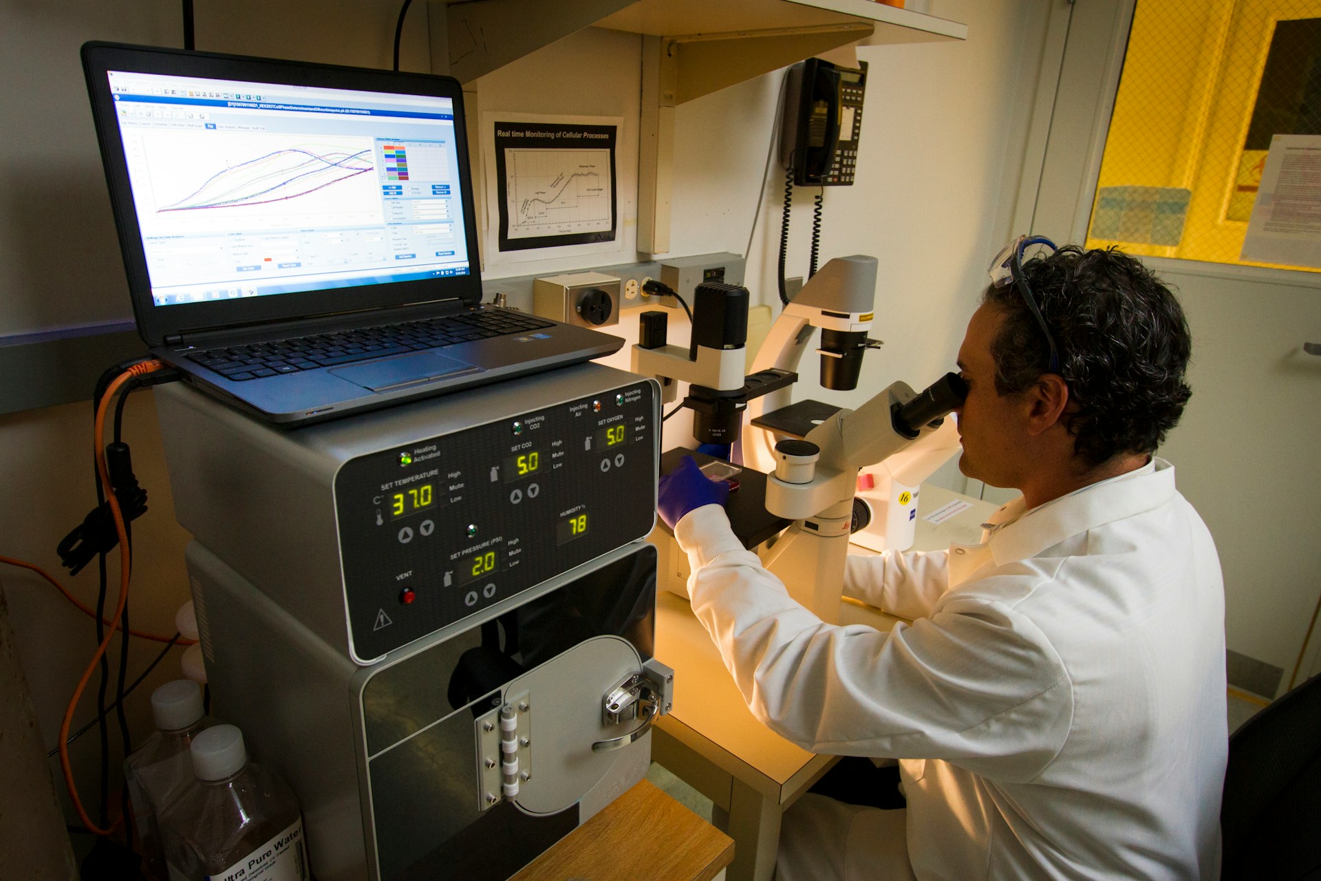 man using computing tech whilst looking in microscope