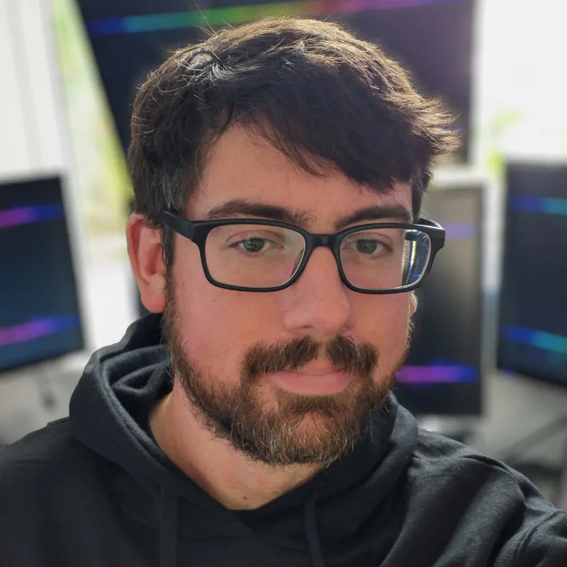 A man in glasses smiles at the camera. This is Robin Wells, Executive Consultant. Behind him are multiple computer monitors.