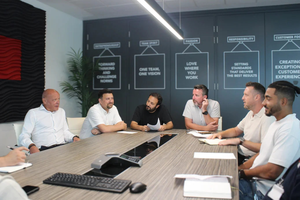 Mane leadership team meeting beneath the company values displayed in the Watford office