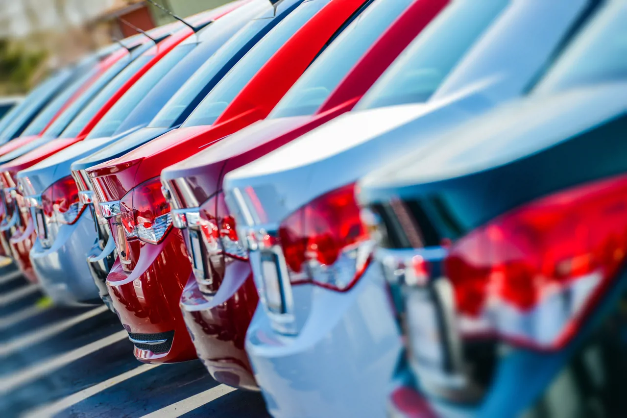 closeup of the back of cars, slightly side on, the cars are a mixture of white, black, grey, silver and red and are lined up in a row