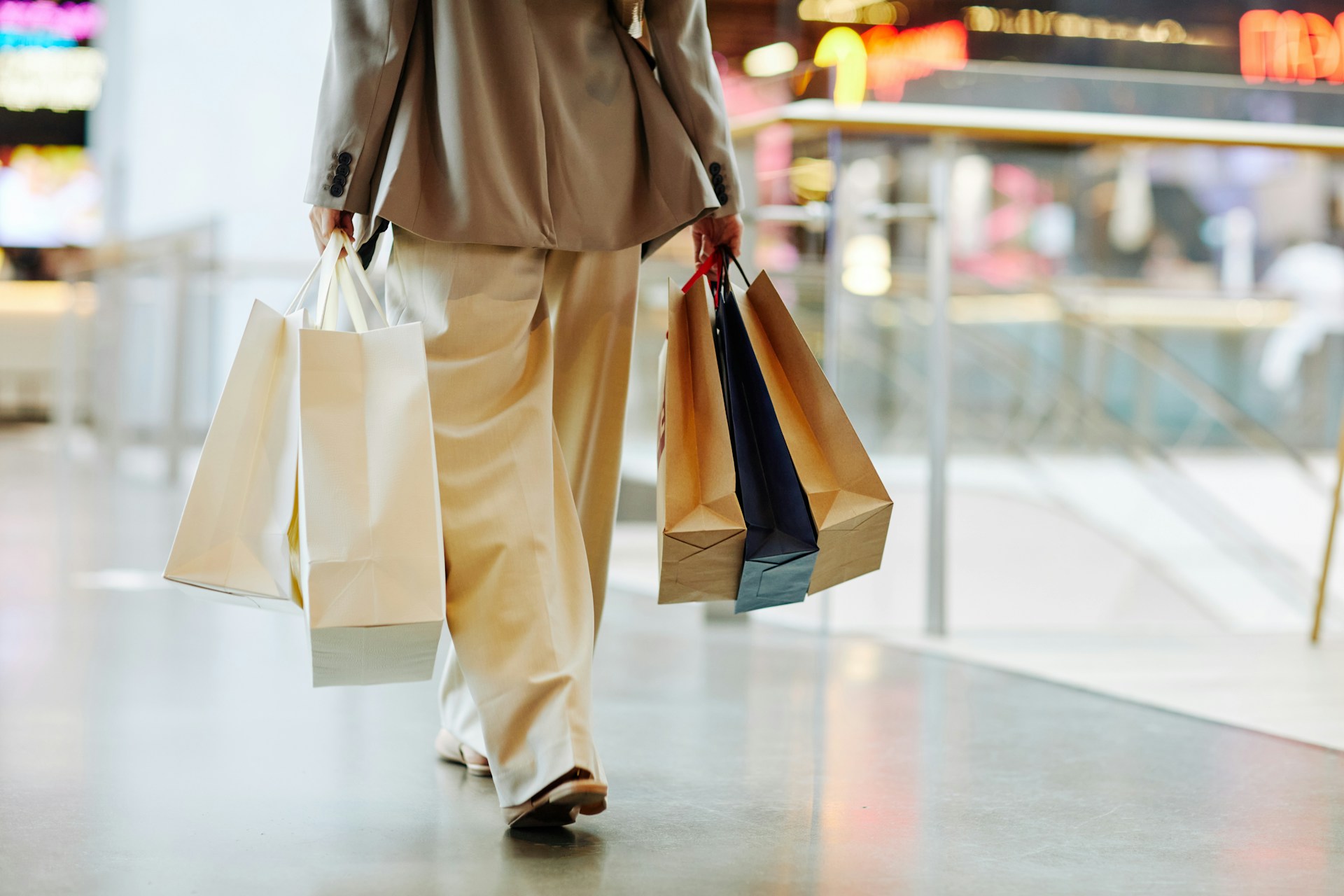 low-section-of-unrecognizable-woman-wearing-pants-and-holding-blank-shopping-bags-while-walking-in-mall-copy-space-