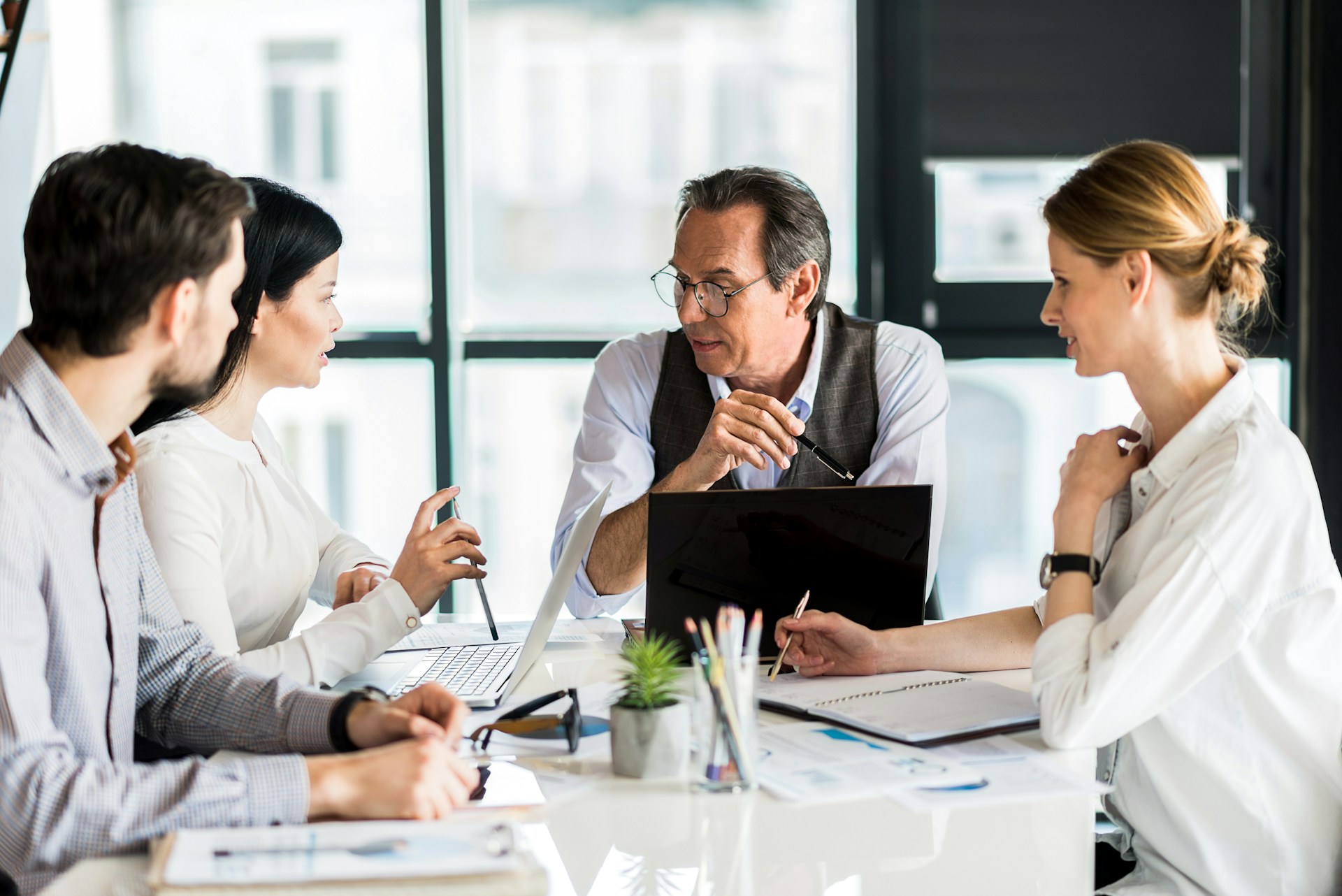 pleasant-work-involved-serious-colleagues-sitting-at-table-while-communicating-together-selective-focus-on-pleasant-mature-man-keeping-pencil-thoughtfully-