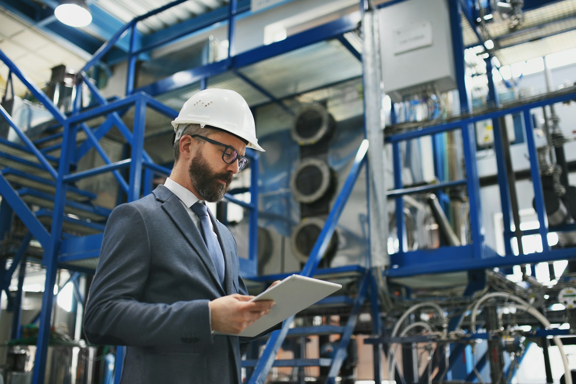 a-chief-engineer-in-the-hard-hat-walks-through-industrial-factory-while-holding-tablet