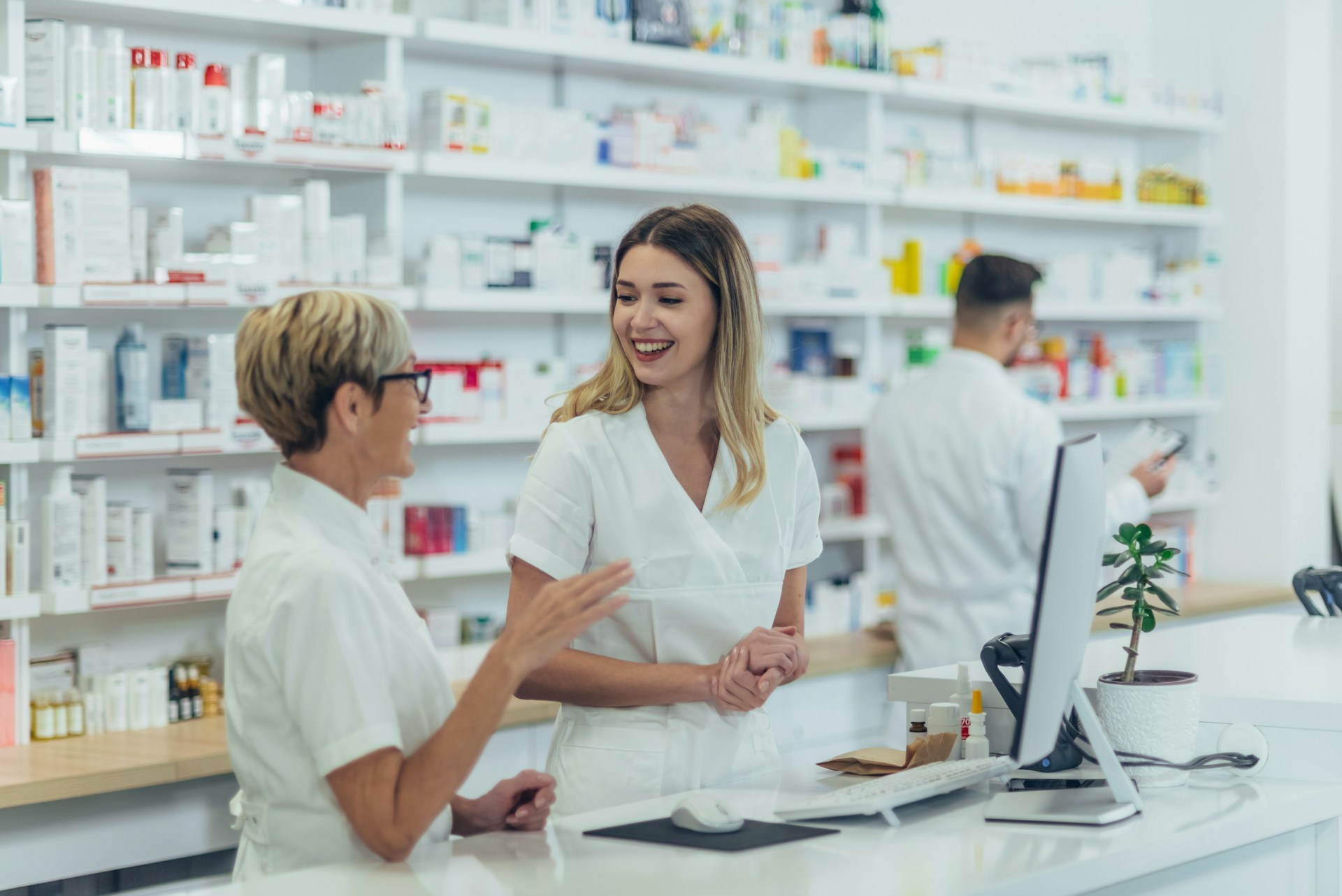 happy-young-female-pharmacist-working-with-senior-colleague-while-standing-near-the-desk-and-talking-