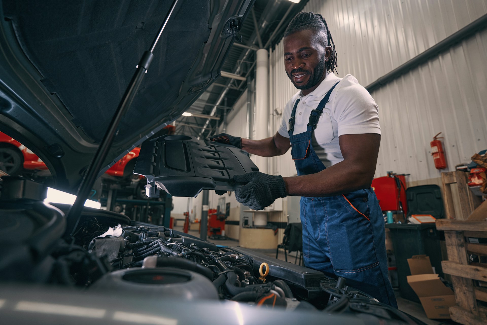 pleased-automotive-technician-removing-protective-cover-from-car-engine-and-looking-at-its-parts