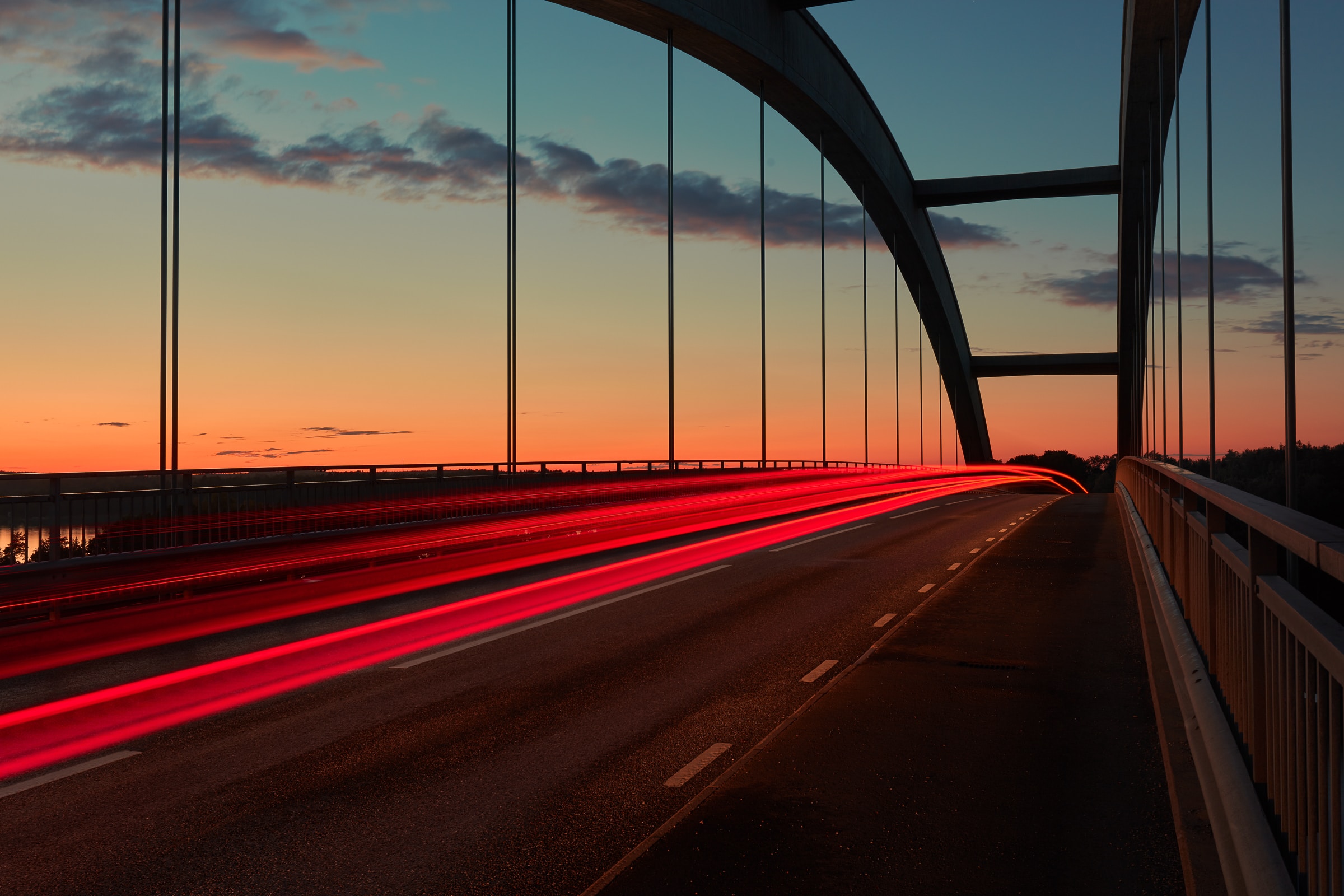 A light-trail photograph shot on a bridge at sunrise of cars’ brake lights as they quickly pass by.