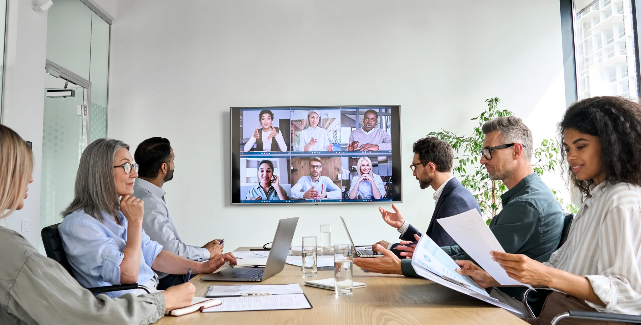 company employees having online business conference video call on tv screen monitor in board meeting room.