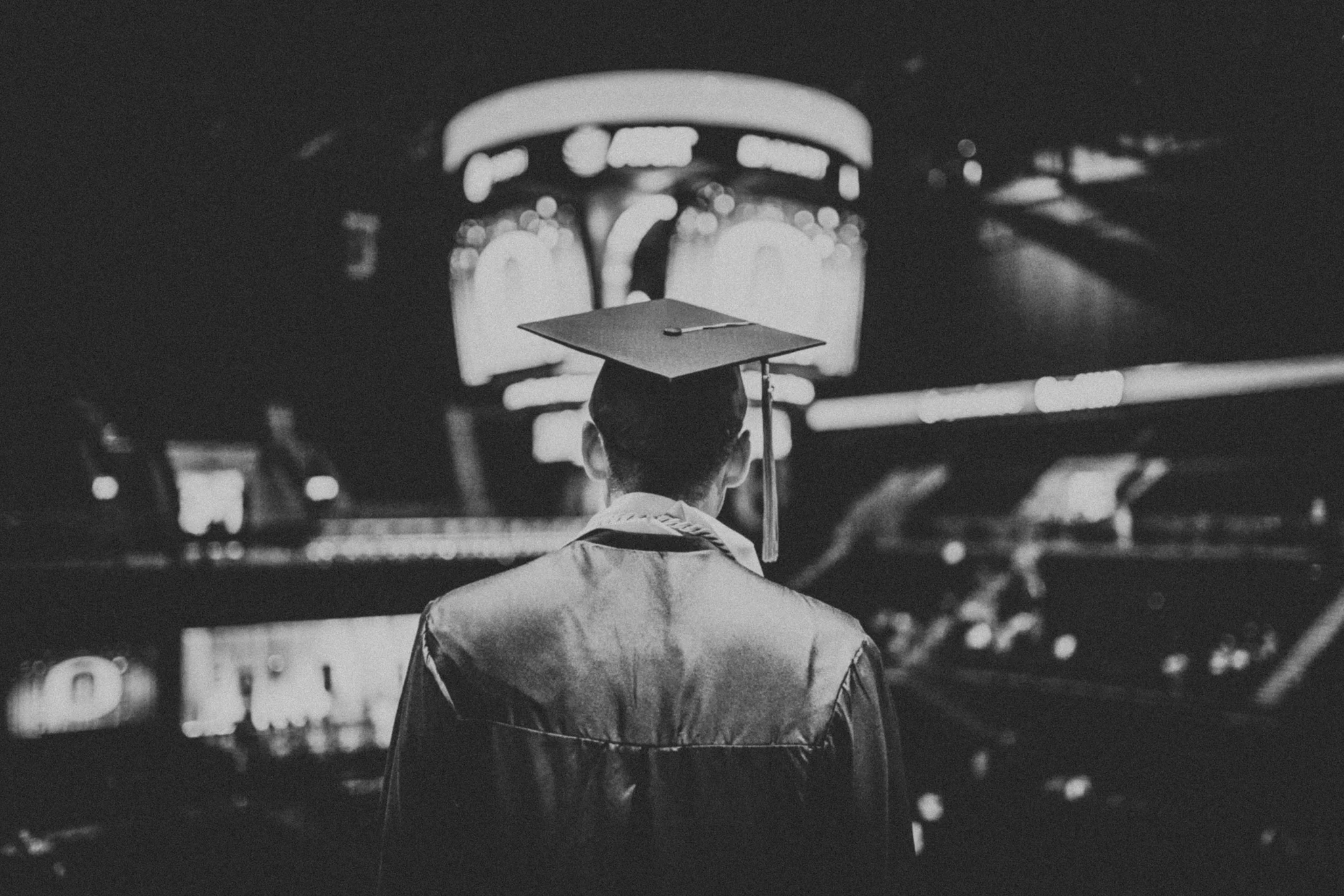 Black and white image of a male graduate from behind with his cap and gown on
