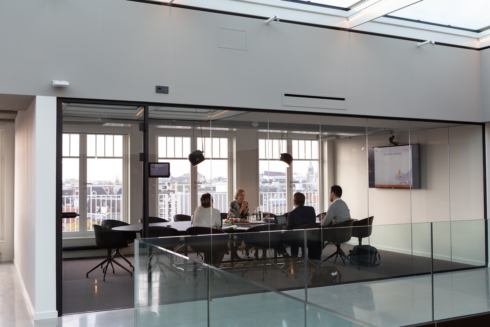 An executive team meets in an open-plan, glass-walled meeting room.