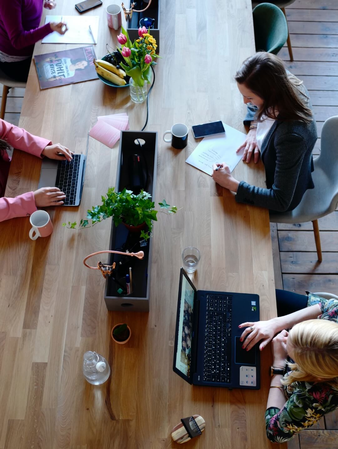 People working at a large wooden desk with laptops