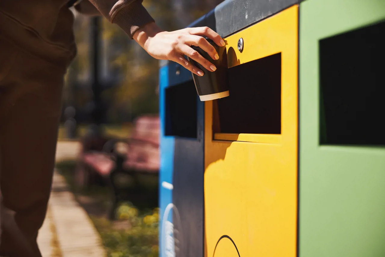 Person throwing away a drink into recycling bins outdoors