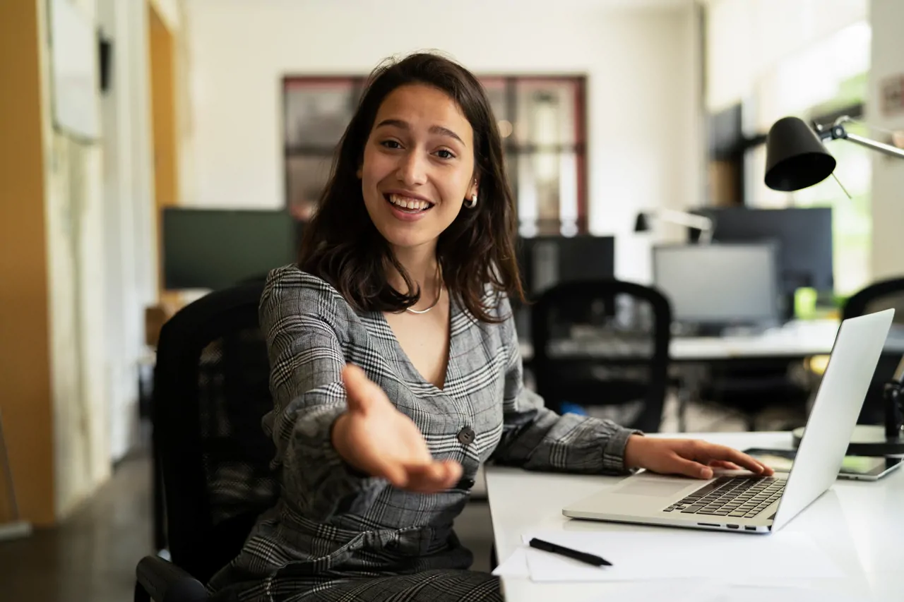 Smiling woman at desk holing out her hand