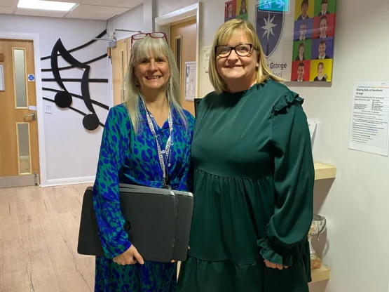 Two women in school corridor holding donated laptops