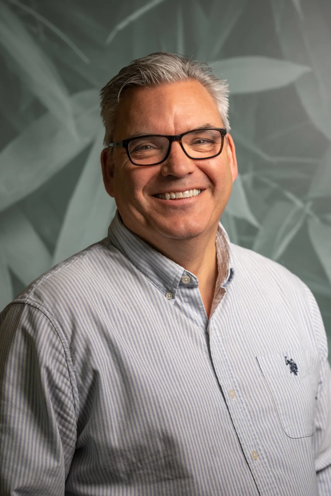 Man in striped Ralph Lauren Polo shirt wearing glasses smiling for headshot photo