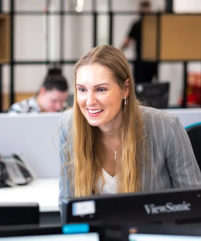 Woman wearing blazer stood looking at computer screen