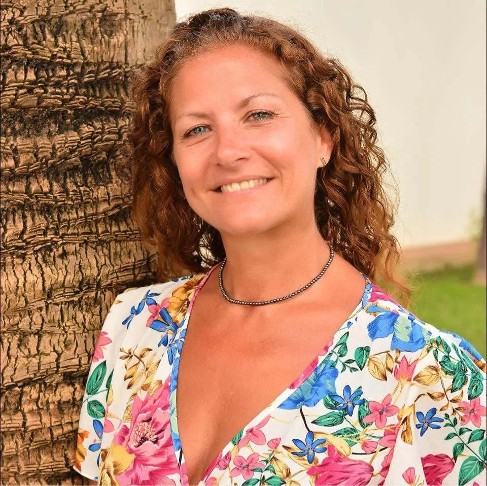 Woman stood next to tree trunk in floral dress smiling for photo