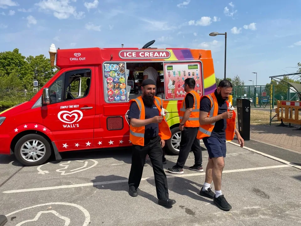 Three men in high vis jackets holding an ice cream cone walking away from ice cream van