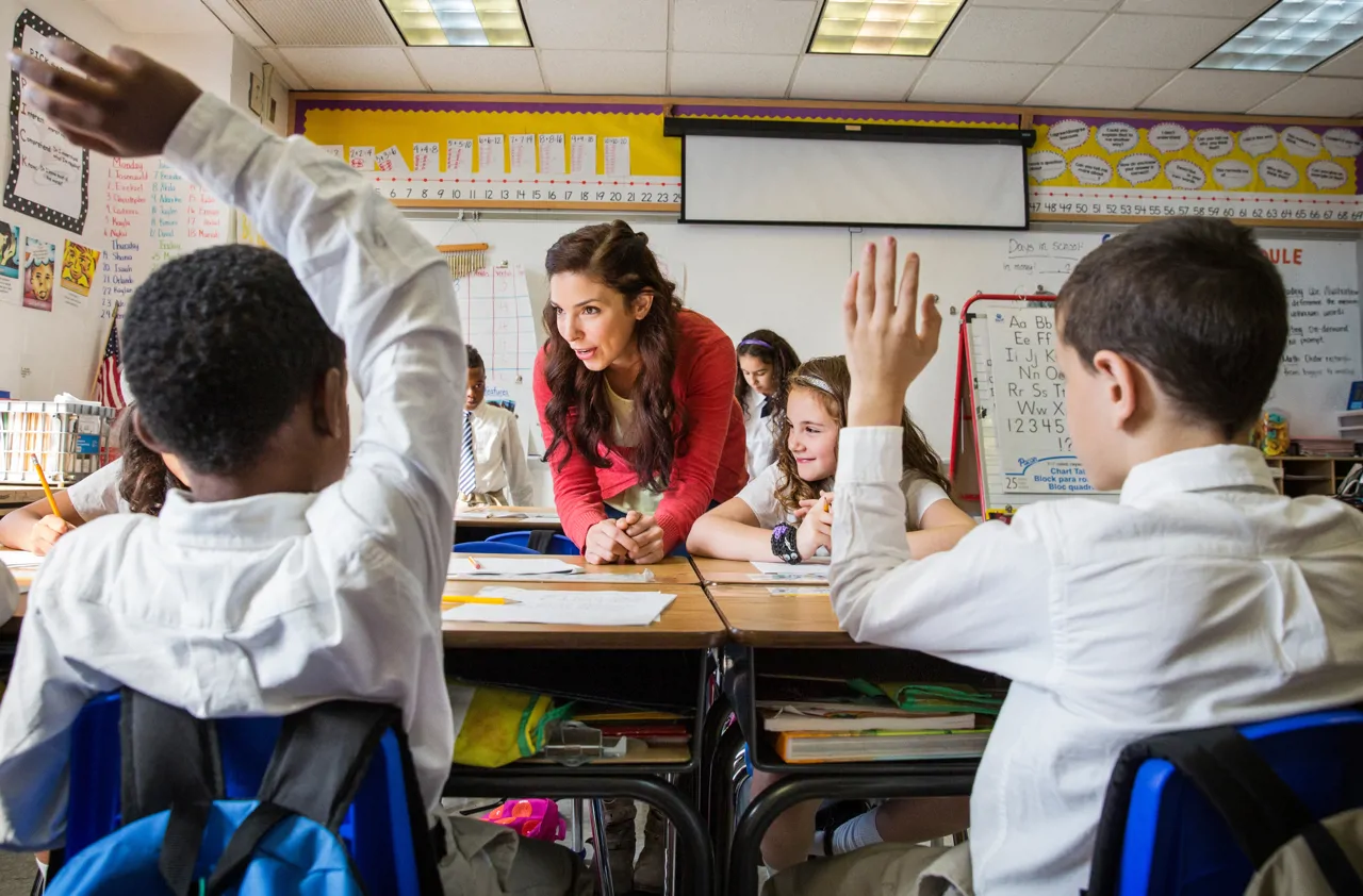 School children raising hands in classroom