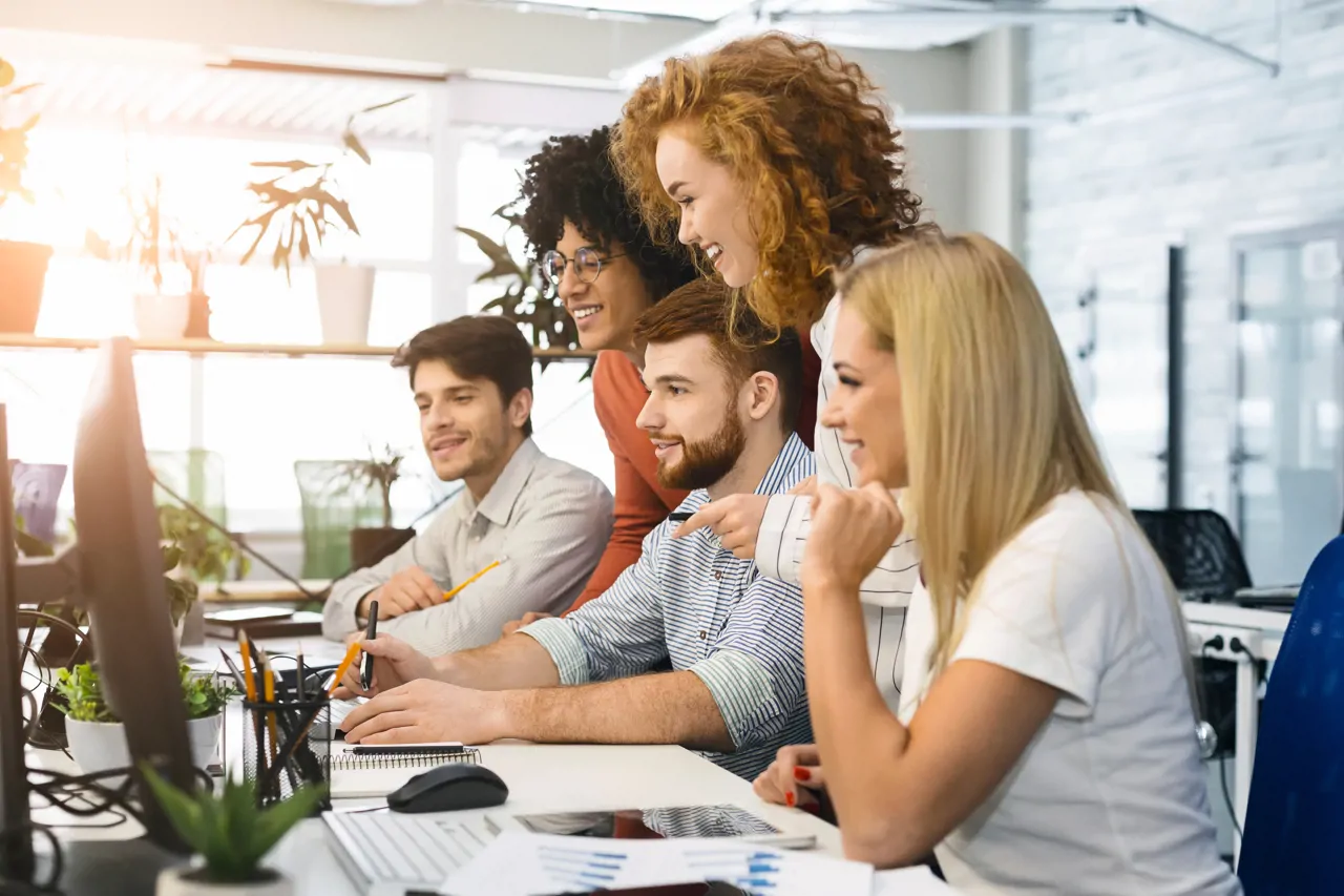 Five young office workers in a colourful office collaborating at a desk 