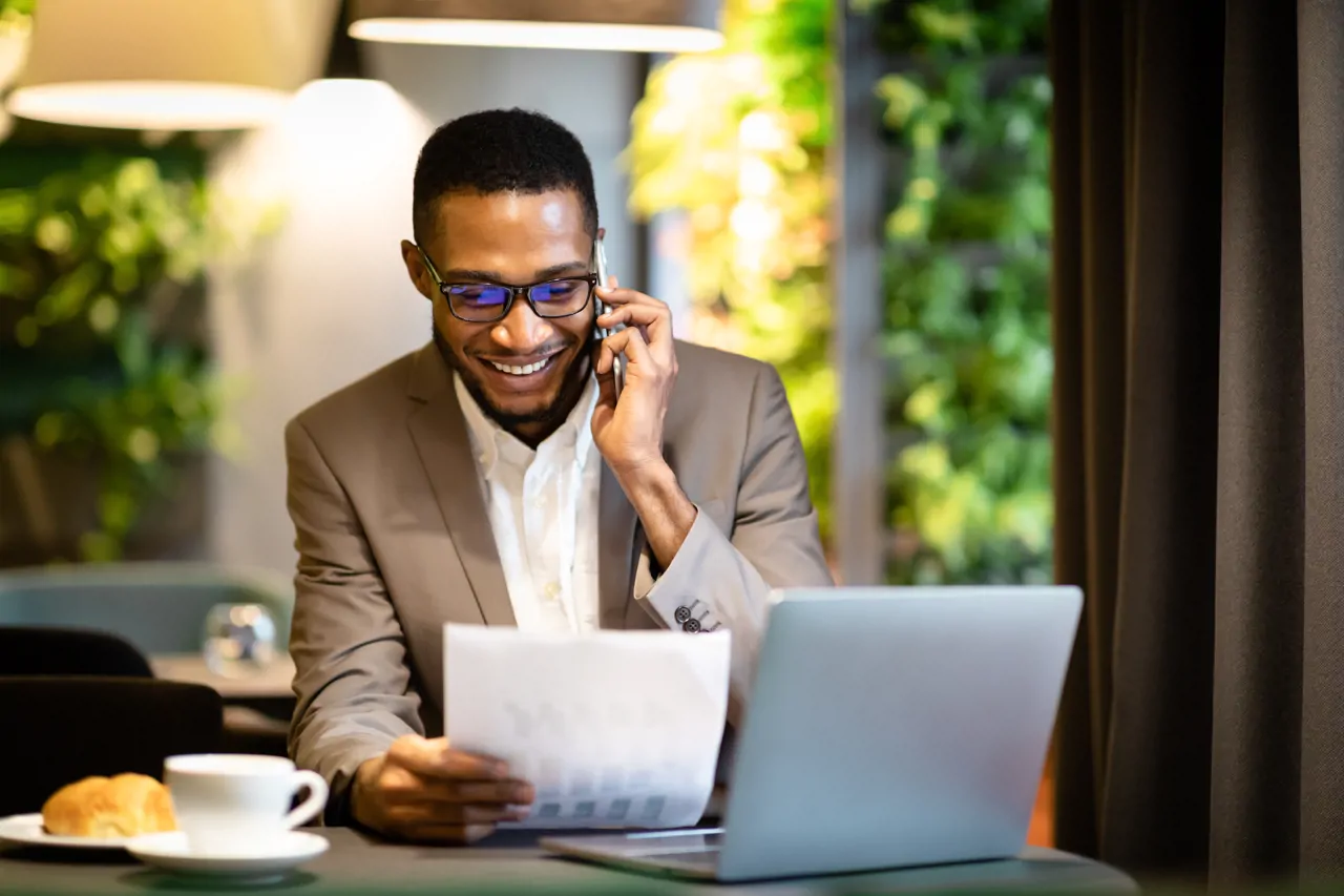 A manreading a piece of paper next to a laptop