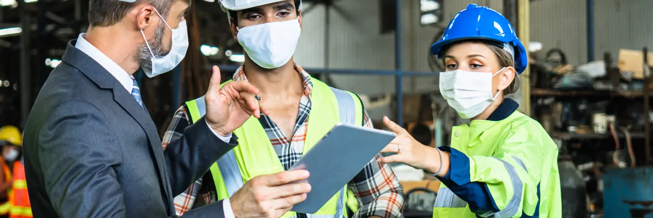 Three people in PPE reviewing information on a tablet