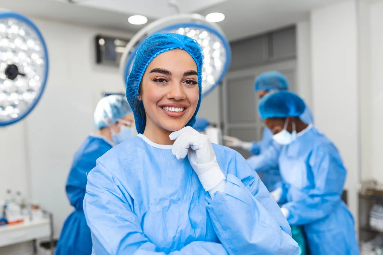 Smiling theatre nurse in scrubs assisting a surgeon during surgery