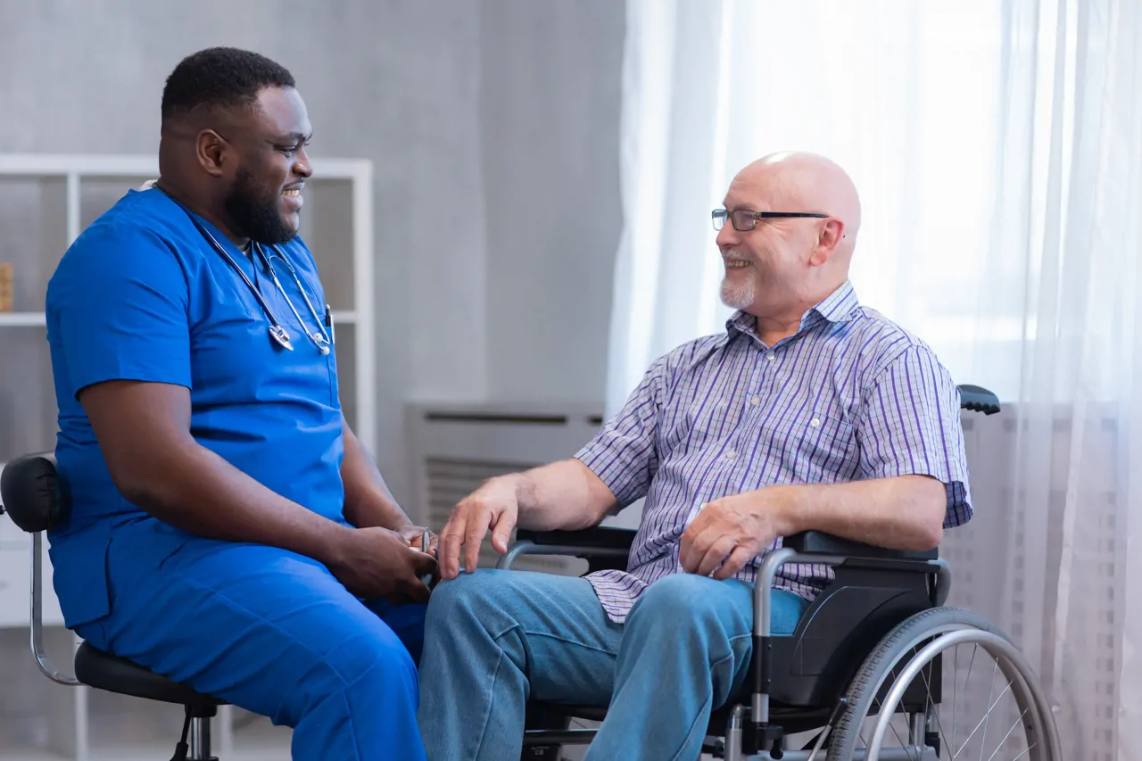 A nurse smiling with a patient in a wheelchair