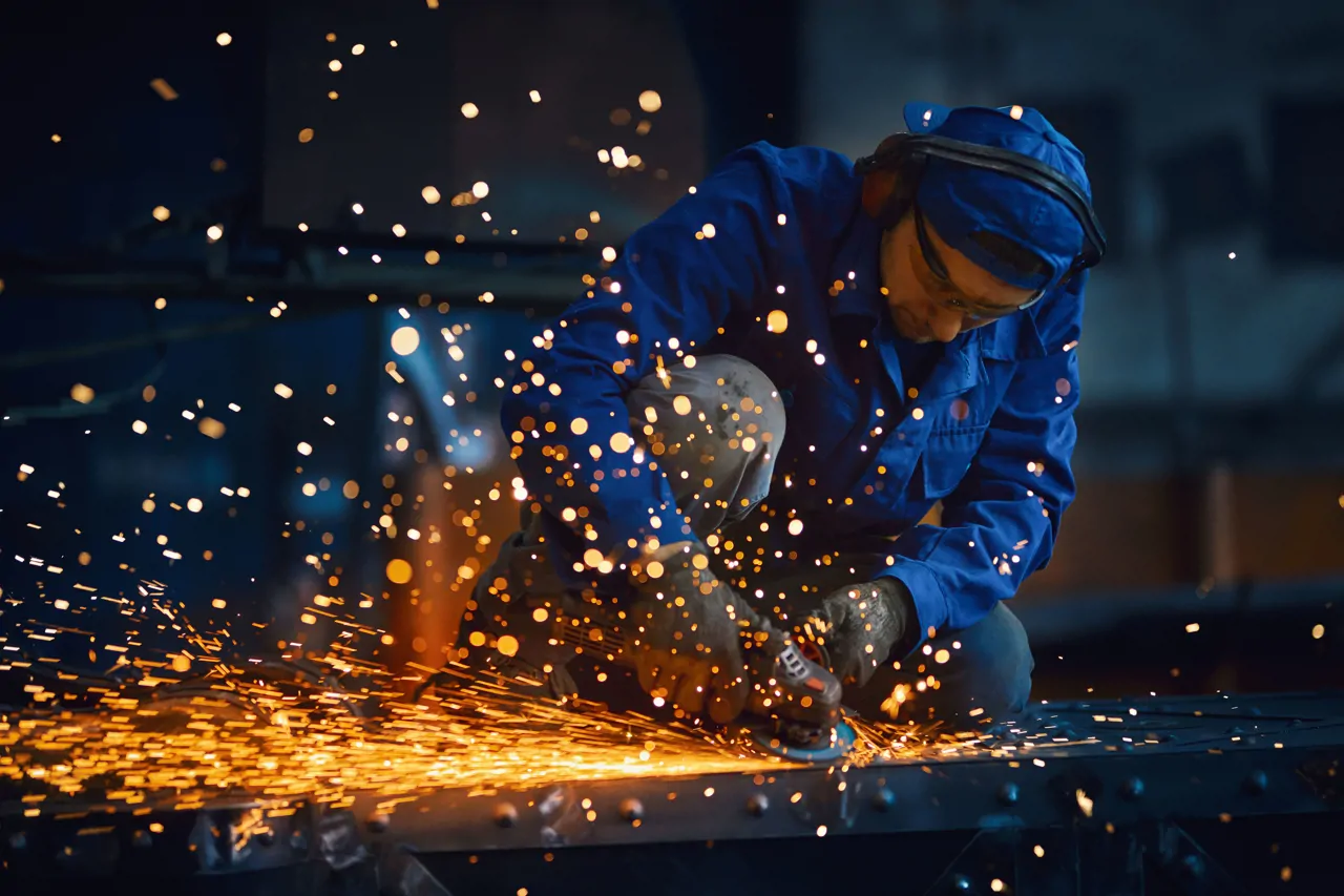 A welder performing a weld on metal, with bright sparks of light illuminating the workspace and creating a dramatic effect.