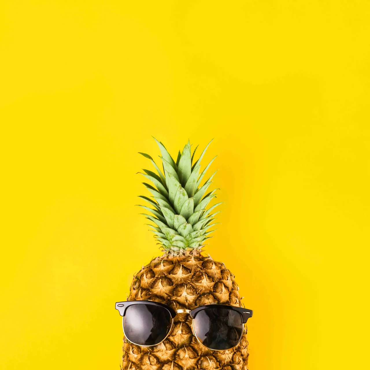 Pineapple on a yellow backdrop wearing sunglasses