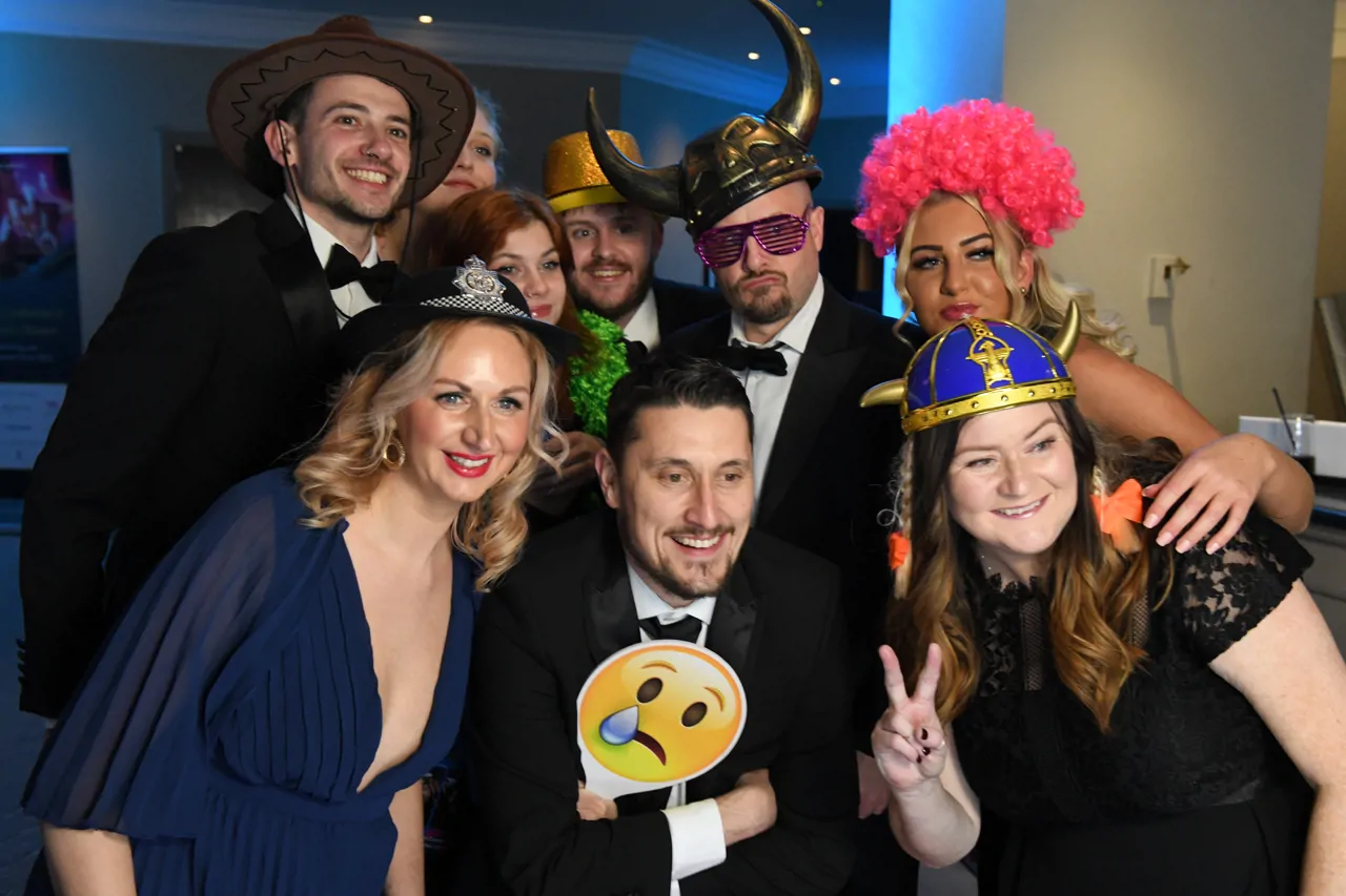 Photobooth shot of group of colleagues at event posing with fancy dress props