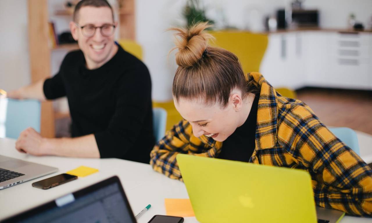 Office professionals laughing together while working on laptops 