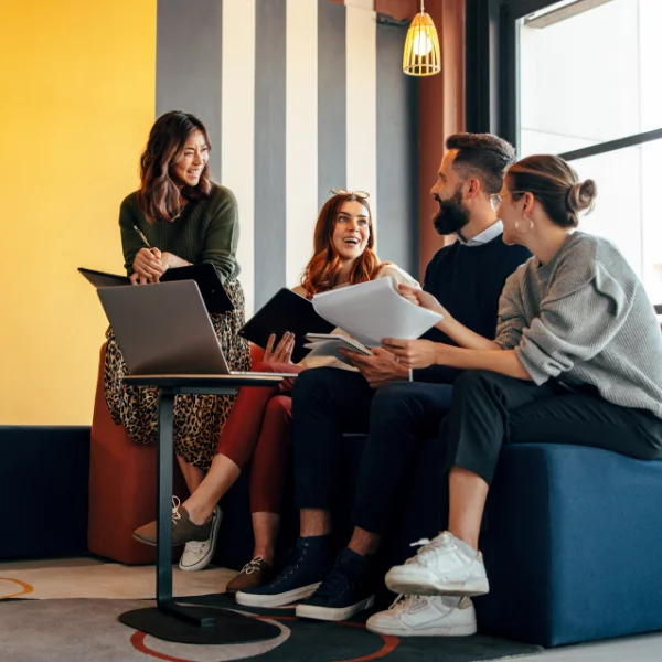 Four young office workers in a colourful office on a sofa laughing