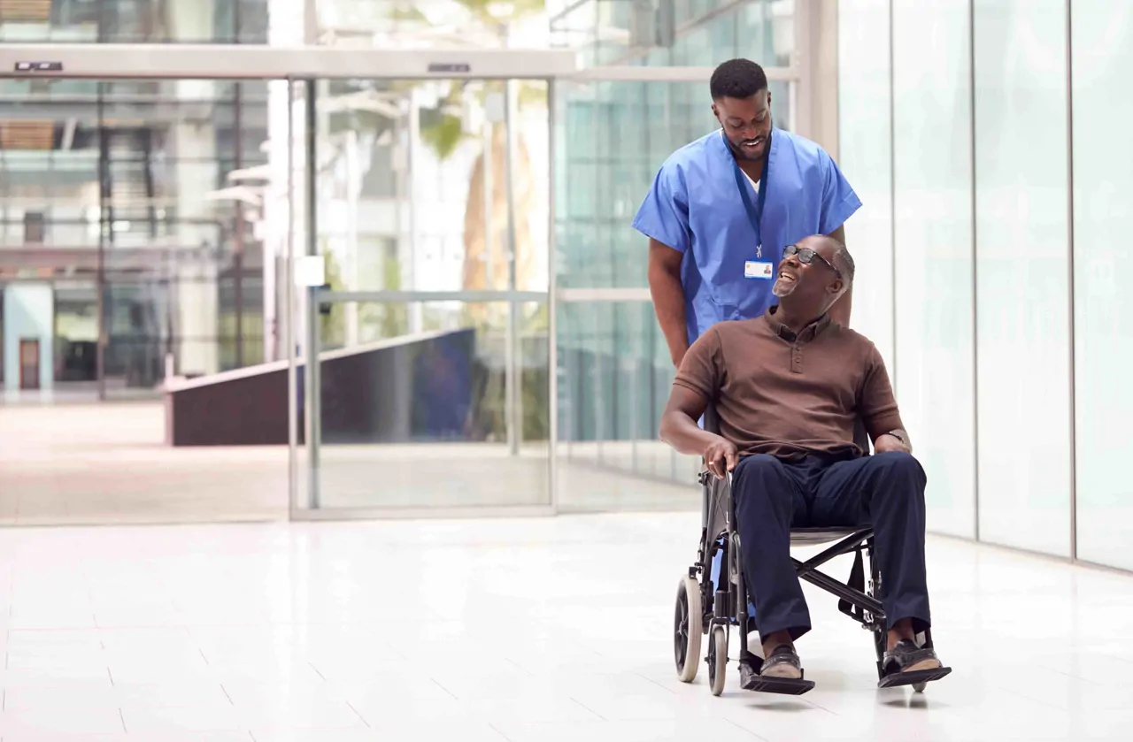 Healthcare professional pushing a patient in a wheelchair down a hospital corridor