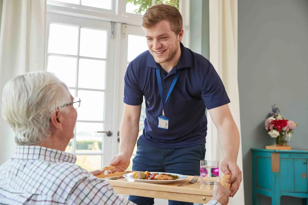 A healthcare assistant bringing a patient his meal