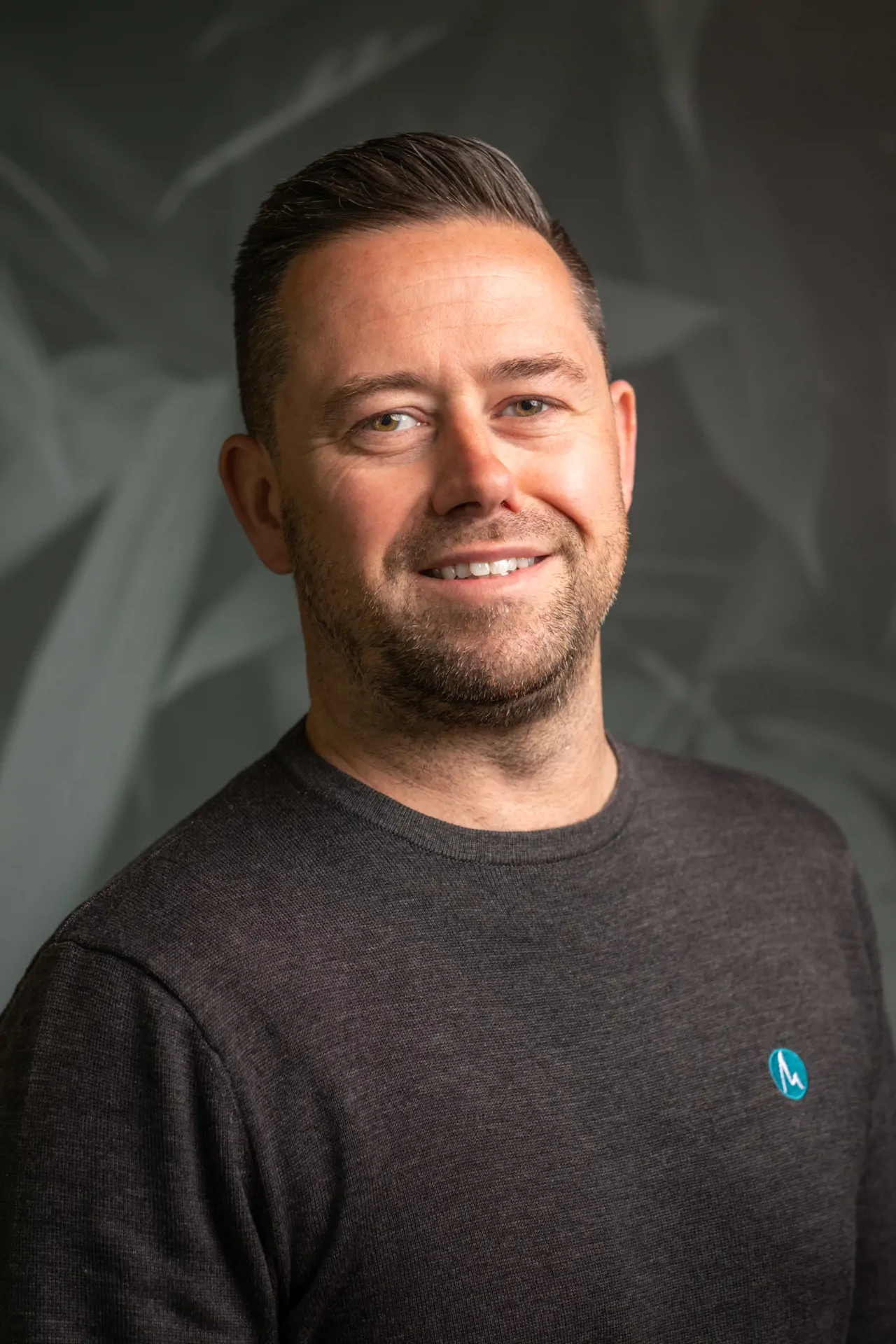 Man with dark hair and stubble smiling for headshot photo