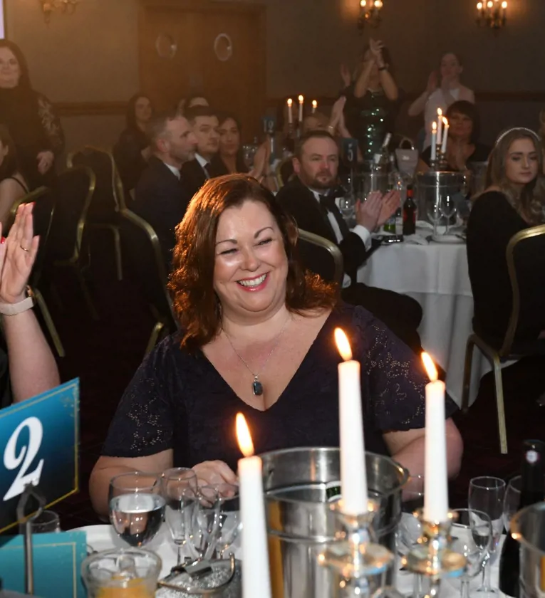 Woman smiling at an awards celebration, with candles on table and a group pf people seated in the background