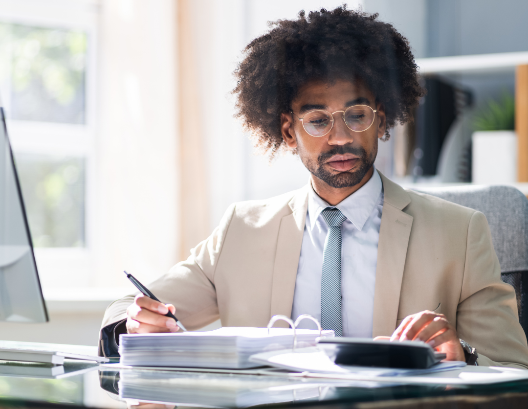 A man sat at a desk with a folder and calculator 