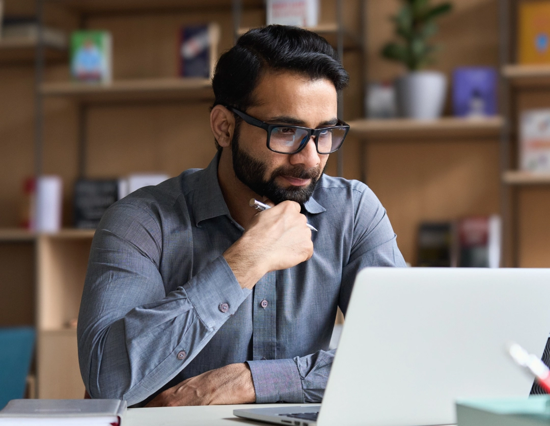 A man wearing glasses looking at a laptop