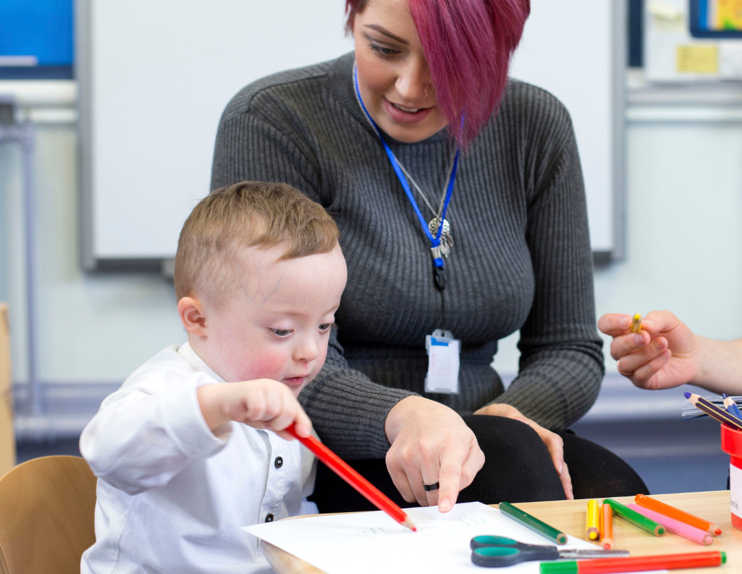 A Teacher helping a young boy colour in