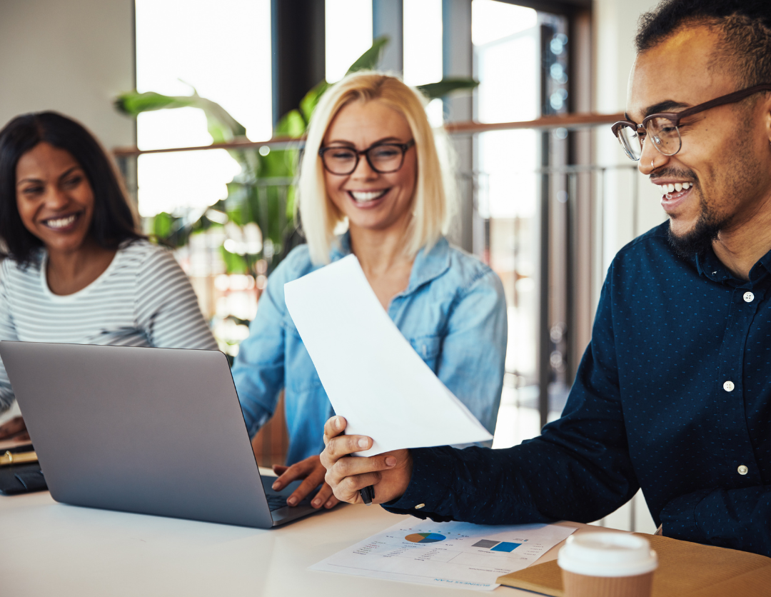 A man and two women sat smiling in front of a laptop