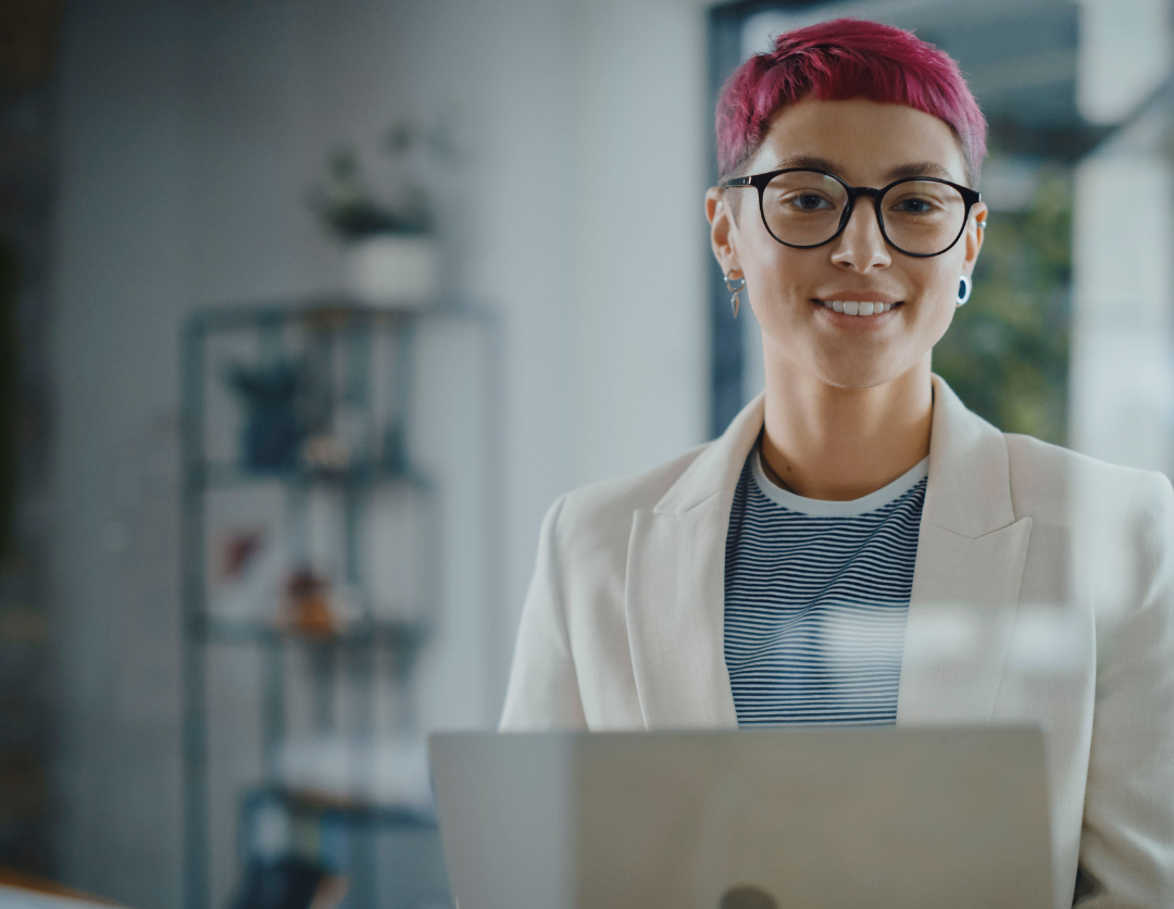 A lady with pink hair stood behind a laptop