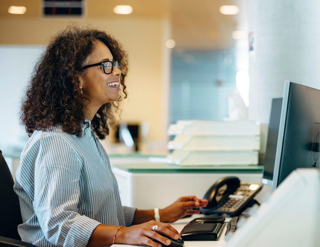 A lady sat at a desk smiling at her computer screen