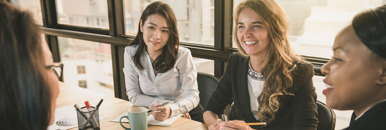  Four women sat around a desk smiling