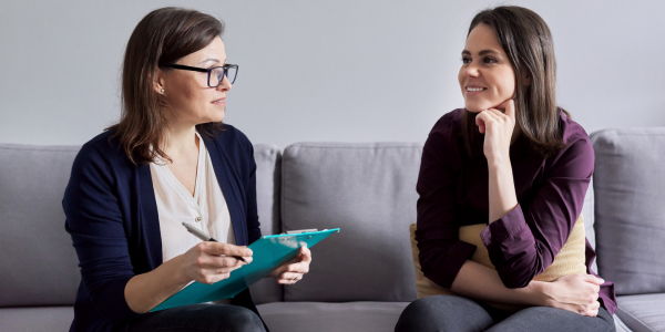 Two females sitting on a sofa, one with a clipbaord