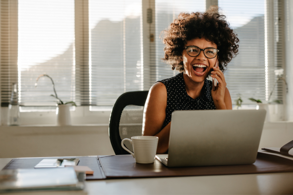 A lady sat at a desk laughing on the phone