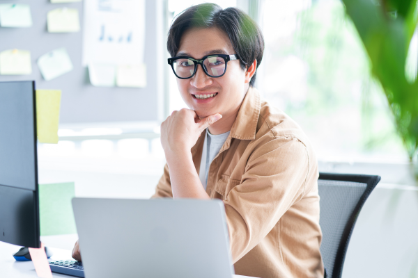 A man smiling at the camera in front of a laptop