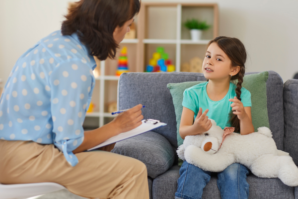 A professional with a clip board and talking to a child. 