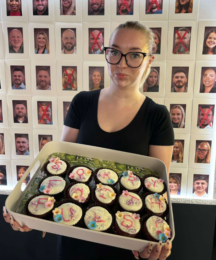 An SCG employee in front of a traitors board, holding cupcakes