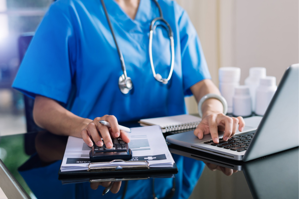 A healthcare professional sat at a desk working with a laptop and calculator